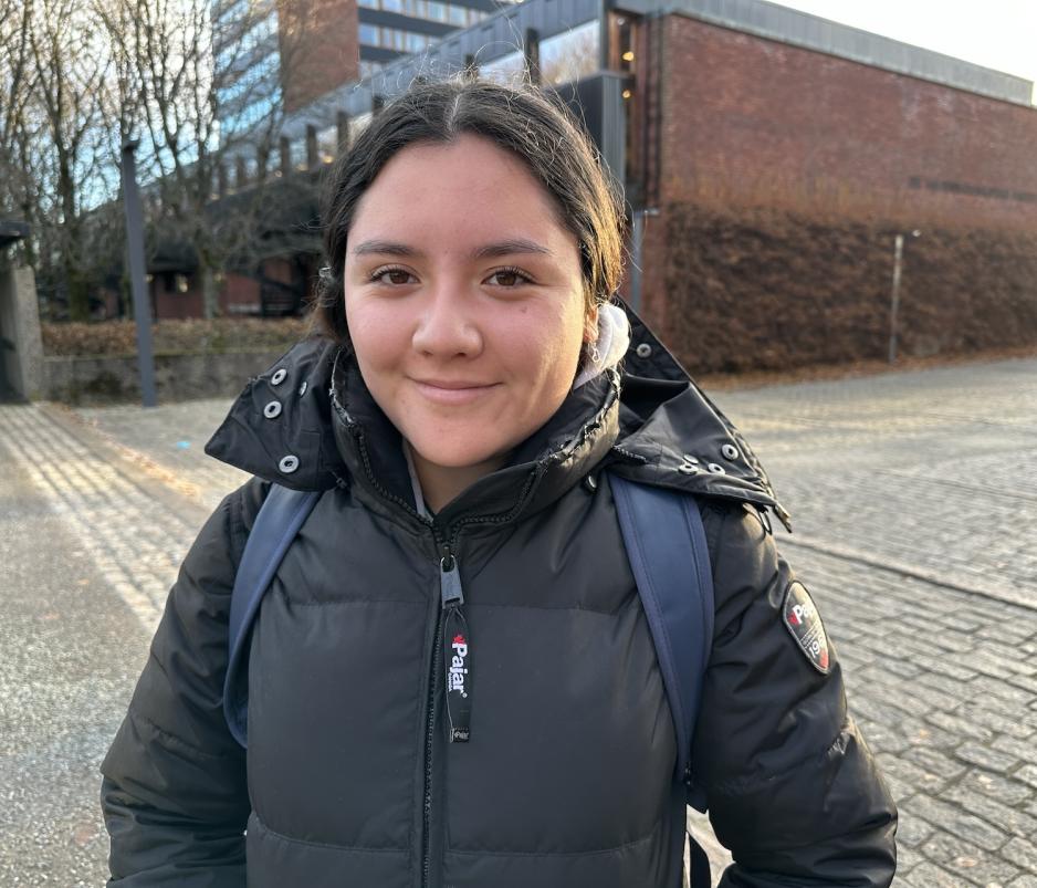 En jente med m&oslash;rkt h&aring;r som smiler mot kamera