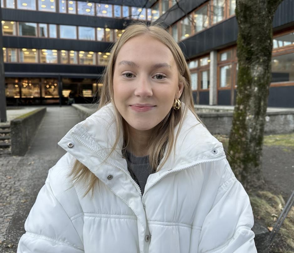 En jente med lyst h&aring;r smiler mot kamera