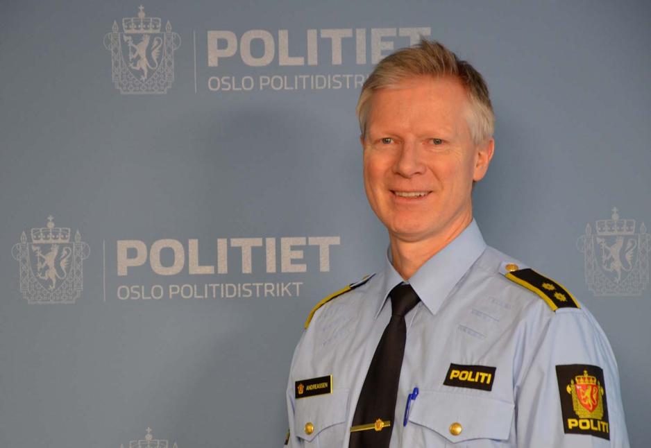 Politmann st&aring;r ved en Politi plakat og smiler