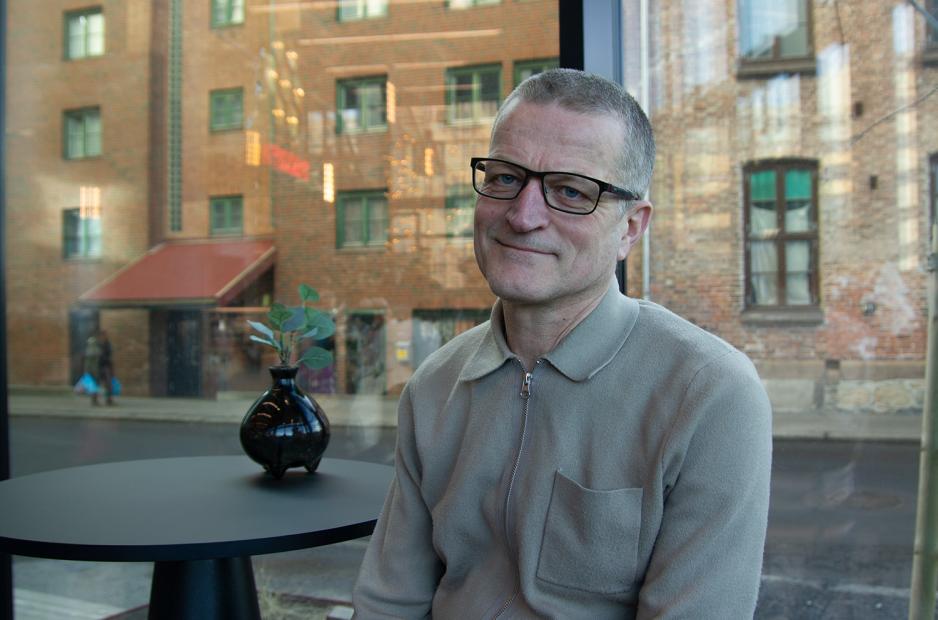 Bildet viser en mann som smiler inn i kamera. Han har briller p&aring;, og sitter p&aring; en h&oslash;y stol.