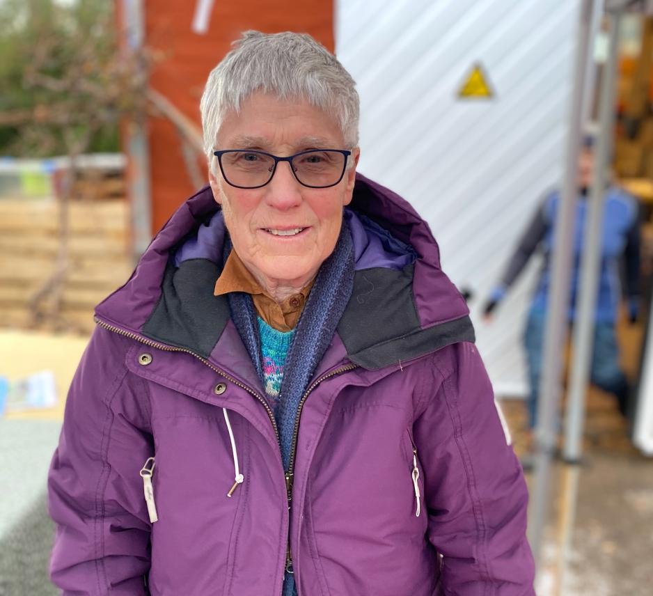 Bildet viser en eldre dame, som smiler til kameraet. Hun har p&aring; seg en lilla jakke.