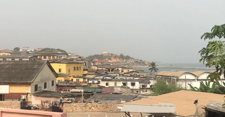 Flere hus vises p&aring; avstand gjennom en gr&oslash;nn skog under en bl&aring; himmel