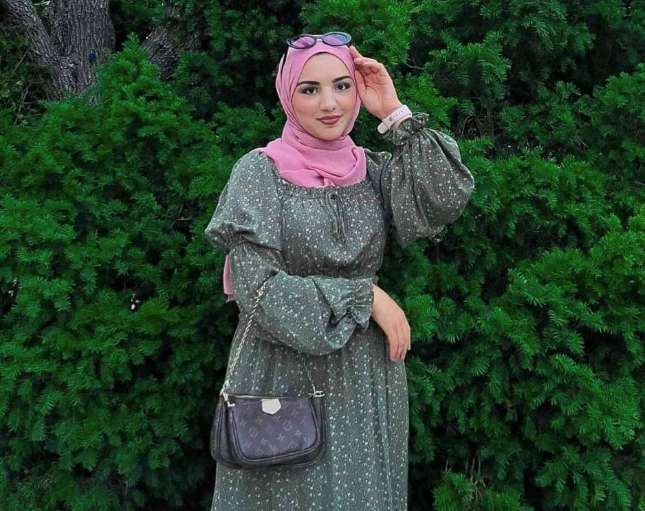 Her ser vi ei dame foran busken som har p&aring; seg en gr&oslash;nn kjole med hvite prikker. P&aring; hodet har hun solbriller og en rosa hijab. Hun holder ei veske i h&aring;nden.