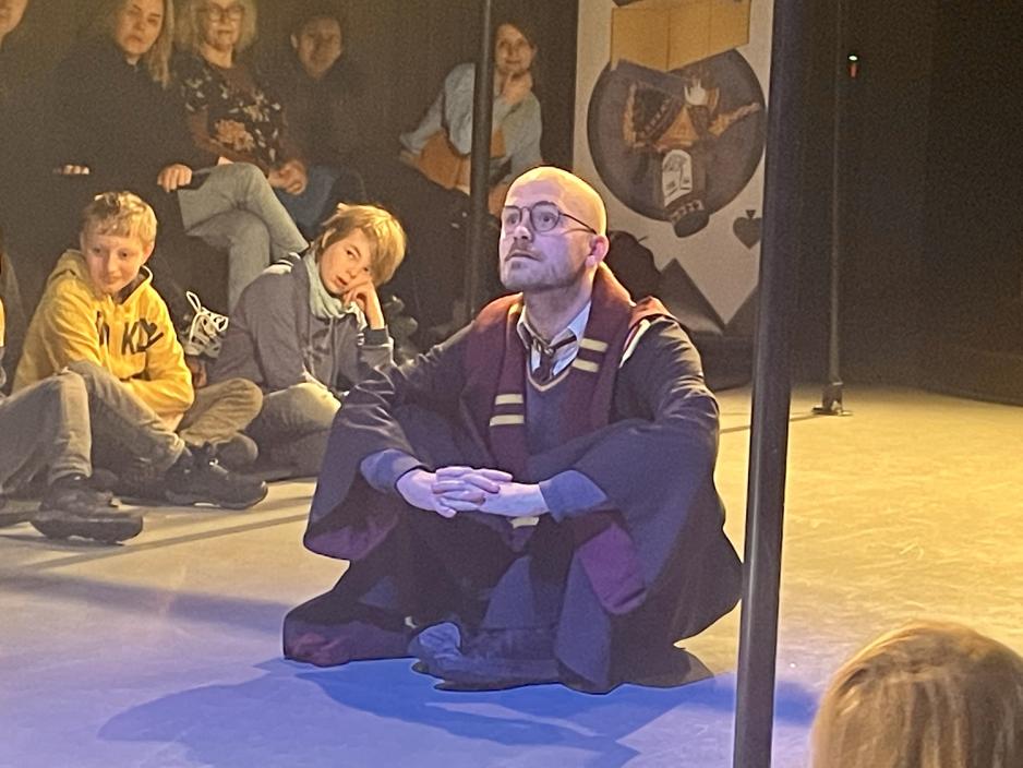 Skallet mann med runde briller og Harry Potter-kostyme sitter p&aring; gulvet med beina i kors og hode hvilende i hendene. 