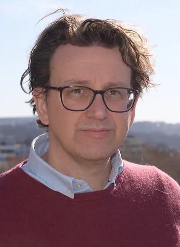 Mann med m&oslash;rkt h&aring;r, briller og r&oslash;d genser.