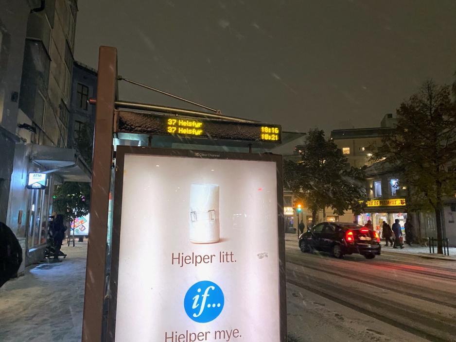 Bildet viser buss-stoppet i T&oslash;yengata i retning 37-Helsfyr. Det er en "if"-reklame, som sier at "if ... hjelper mye". Det er en bil som kj&oslash;rer forbi. Det er m&oslash;rkt ute, og sn&oslash;en faller.