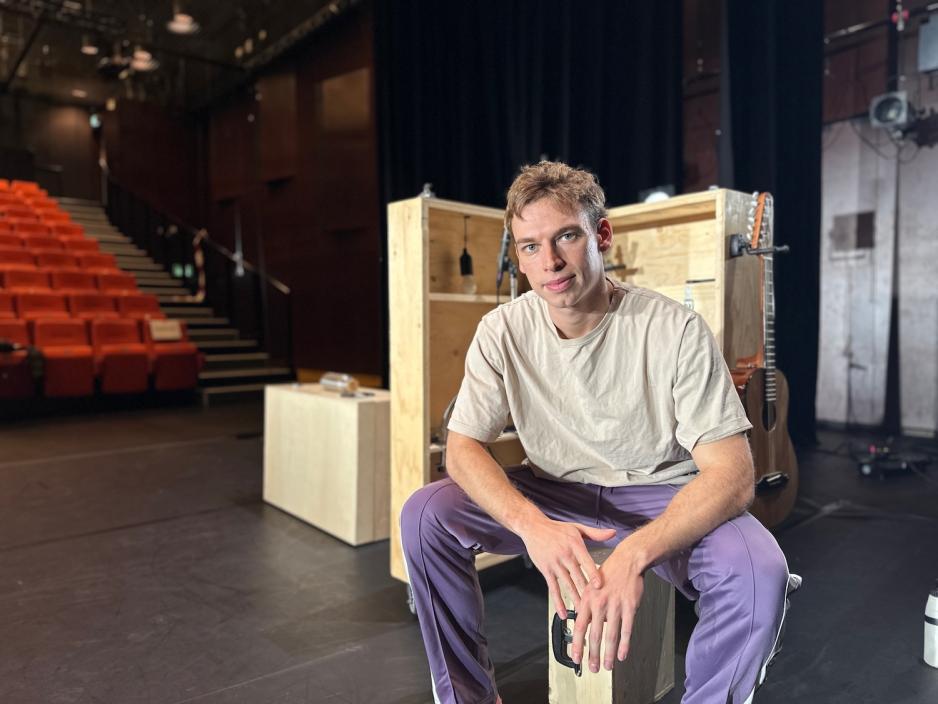 En av skuespillerne i kompaniet sitter p&aring; scenen i en sal uten publikum.