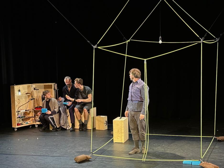 Bilde av scenen. En mann st&aring;r alene inni et hus og kikker ut p&aring; vennene hans som st&aring;r sammen p&aring; utsiden.