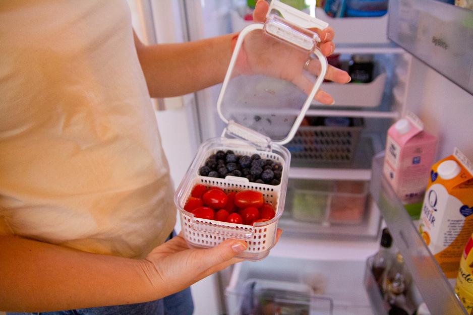 En dame viser fram en boks i kj&oslash;leskapet hennes med tomater og bl&aring;b&aelig;r. 