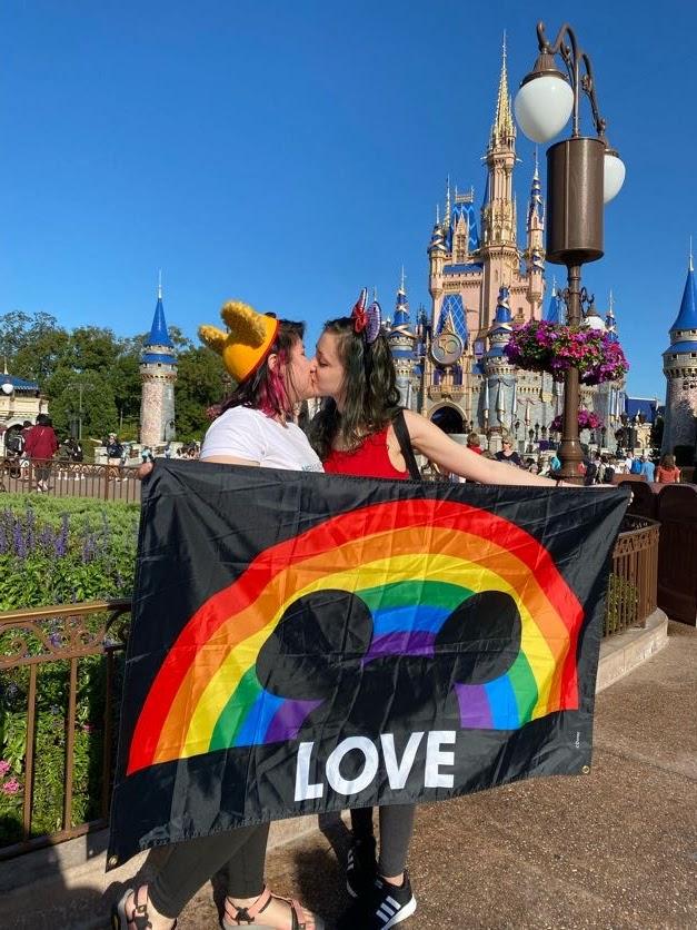 To kvinner st&aring;r med et Disney-regnbueflagg og kysser.