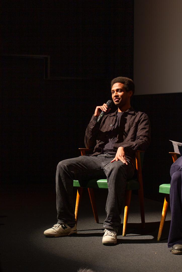 Abdinor Mahamed fotografert p&aring; panelsamtalen etter visningen av dokumentaren. Han er ikledd svarte kl&aelig;r og holder mikrofonen til munnen.