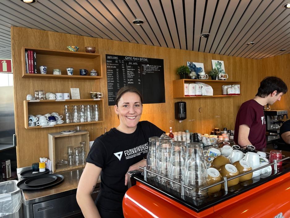 Dame som smiler, st&aring;r ved kaffemaskin