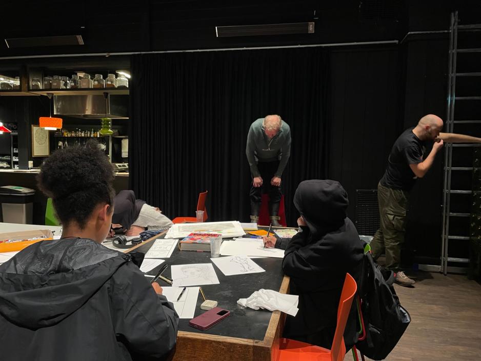 En av spr&aring;kpedagogene st&aring;r p&aring; en stol, mens ungdommene skal tegne han.