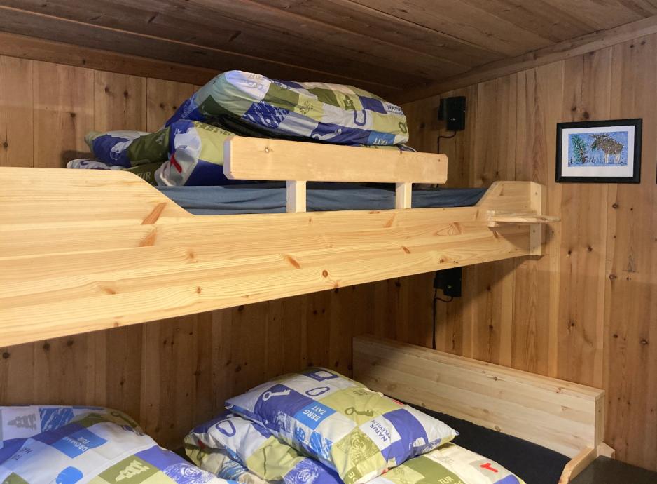 K&oslash;yesenger i tre, med trevegger og bilder p&aring; veggene. Det er bl&aring; og gr&oslash;nne dyner og puter brettet sammen i sengene. 