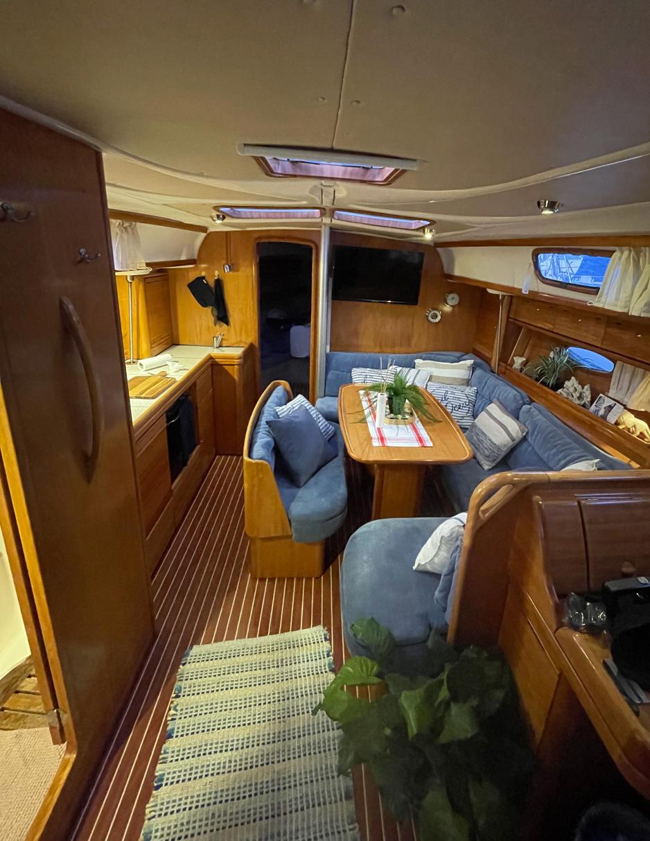 Innsiden av seilb&aring;ten er dekket av brunt treverk. Til h&oslash;yre er det en sittegruppe som er drukket i bl&aring;tt stoff og til venstre er det et lite kj&oslash;kken med brune skapfronter. Gulvet er dekket i vegg til vegg teppe i en lys beige farge.