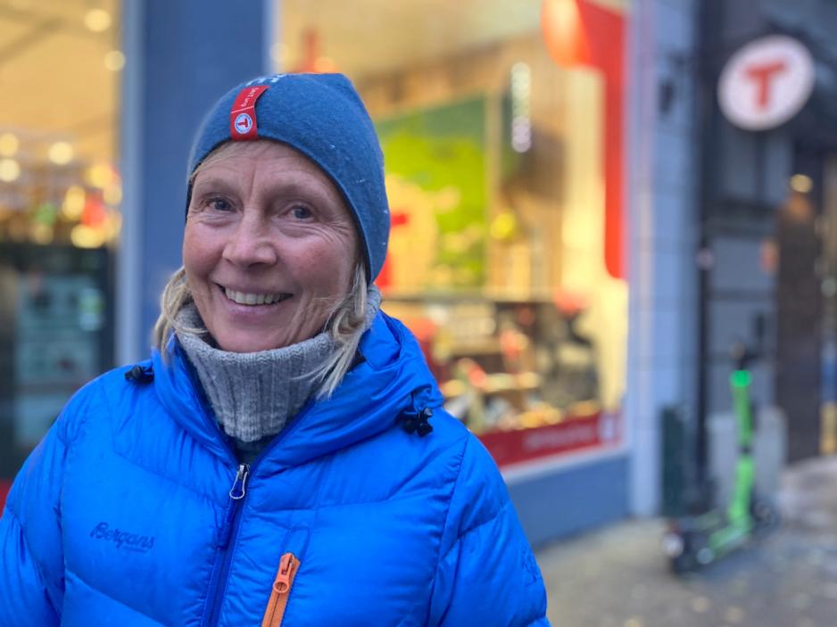 Janet Bydal st&aring;r i turkl&aelig;r foran en DNT-butikk ved Karl Johan i Oslo. Hun smiler og det har skumret ute. 