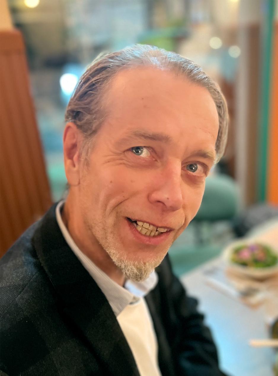 Portrettbilde av en smilende John Tvedt med gr&aring;tt dratt bak, og hvitt skjegg p&aring; haken