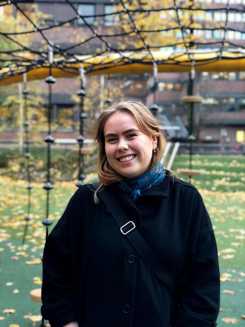 kvinne st&aring;r ute med gule blader og h&oslash;stlandskap i bakgrunnen