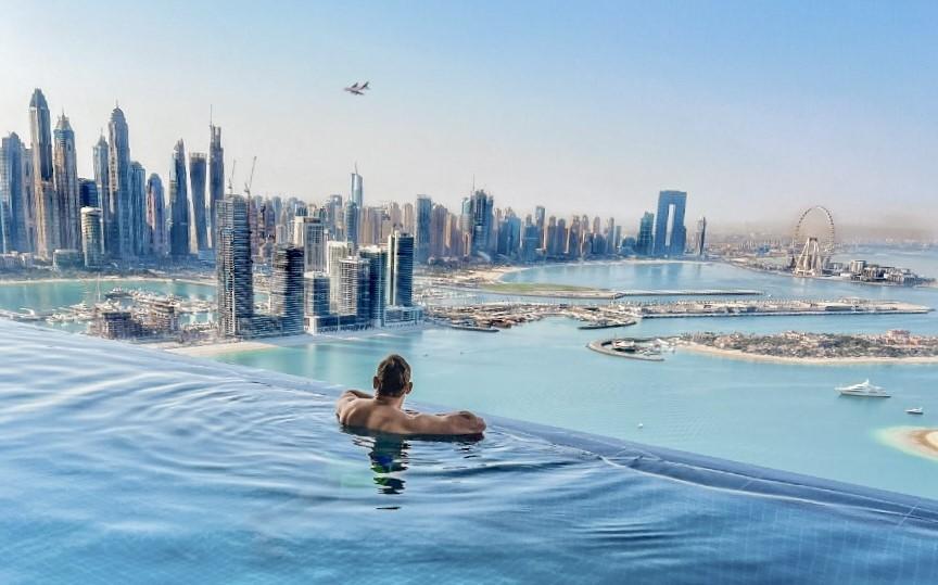 Skallet mann ser ut over Dubai fra et sv&oslash;mmebasseng