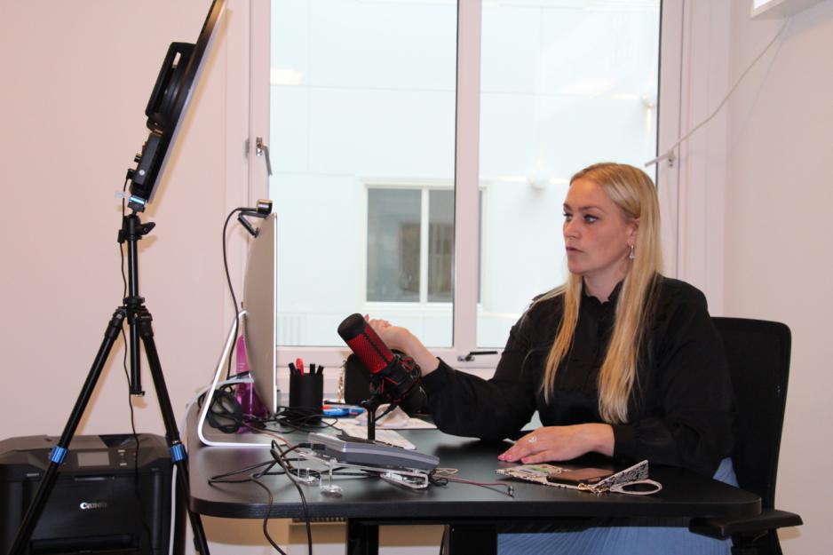 Blond kvinne siter ved pulten og viser noe p&aring; Mac-en. 