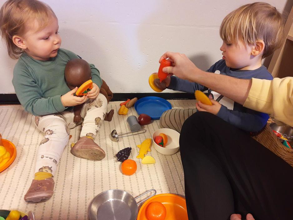 mann sitter p&aring; gulvet med barn rundt. han har en leke-ketchupflaske og tar p&aring; ketchup p&aring; lekematen til barna.