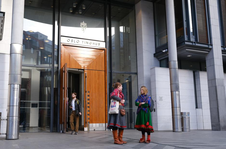 Bilde av inngangen til Oslo tinghus, p&aring; avstand. En mann g&aring;r ut av inngangen og to koftekledde kvinner st&aring;r foran inngangen.
