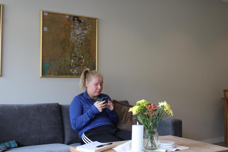 Kristin Hauglid sitter med telefonen i henda, og scroller p&aring; mobilen. Hun sitter i sofaen i stua.