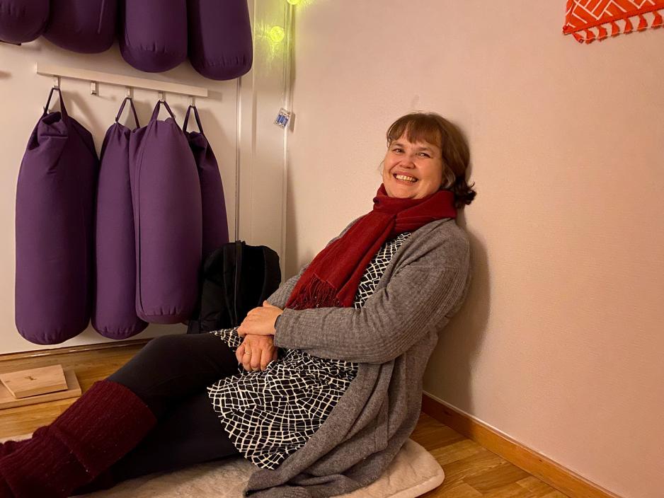 En kvinne sitter og lener seg mot veggen mens hun smiler til kamera