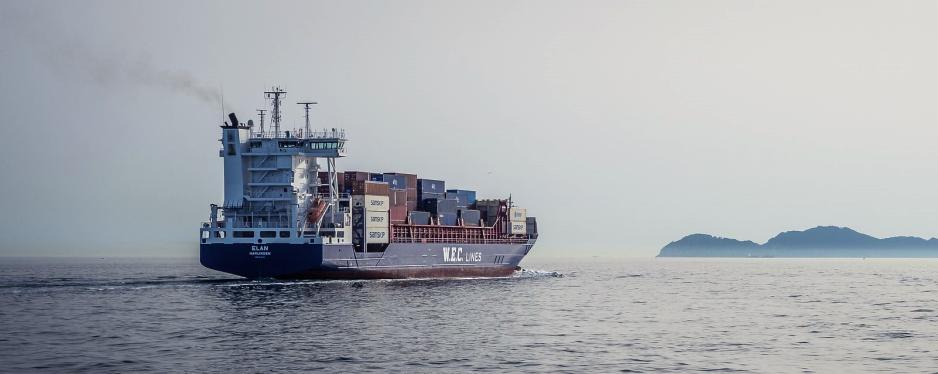 Lasteskip p&aring; &aring;pent hav. Svak gr&aring; sky av eksos f&oslash;lger skipet. 