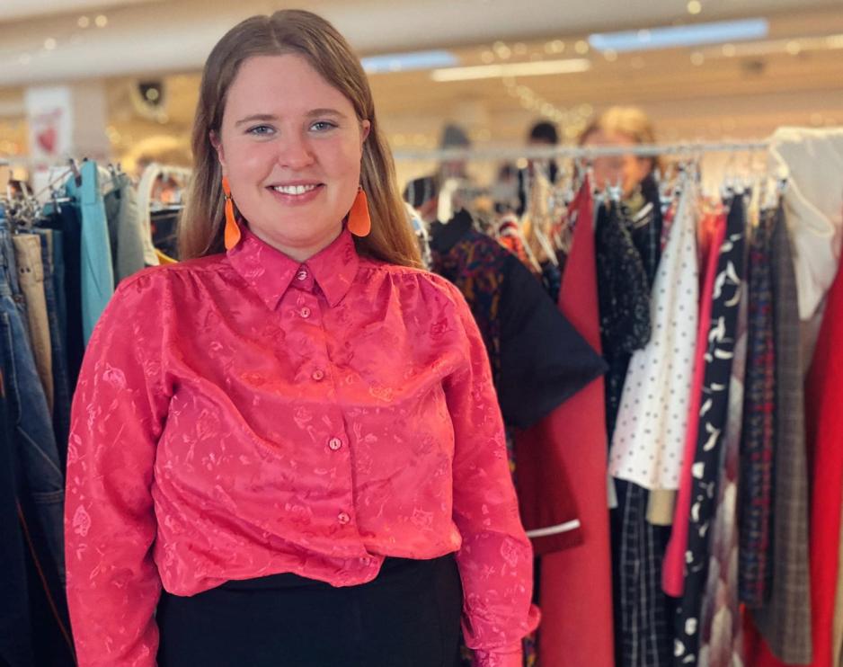 Ei dame som har p&aring; seg en rosa skjorte. Hun har oransje &oslash;redobber og smiler til kamera. 