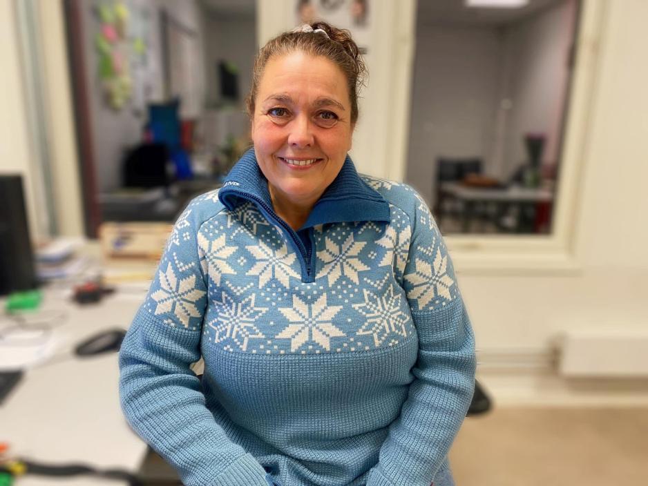 Ei dame som sitter og har p&aring; seg en lysebl&aring; genser med hvite sn&oslash;fnugg. 