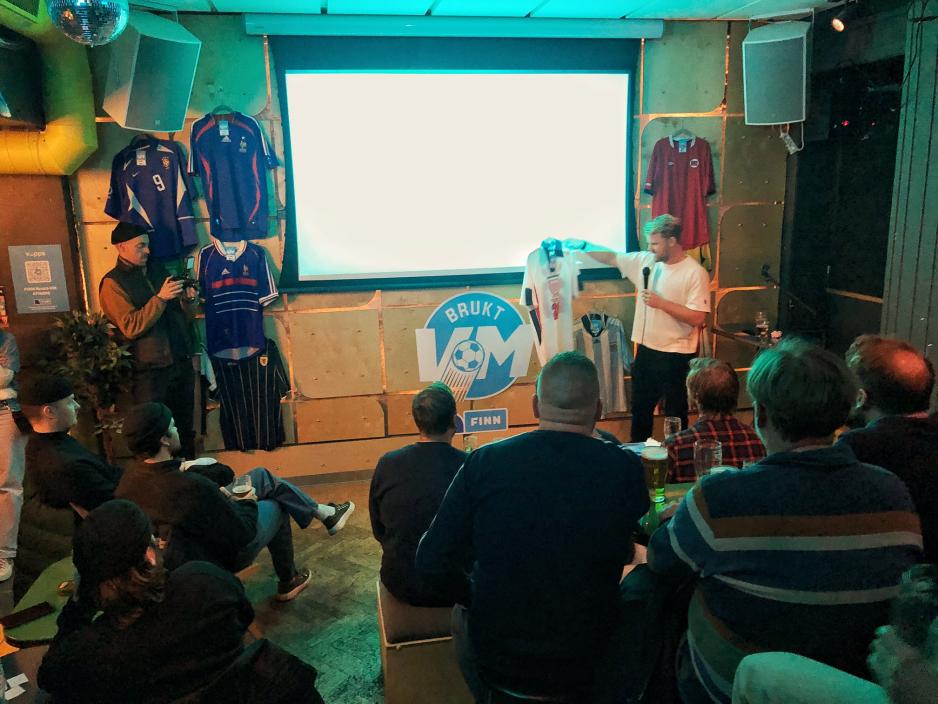 Mann snakker i en mikrofon p&aring; en bar foran publikum