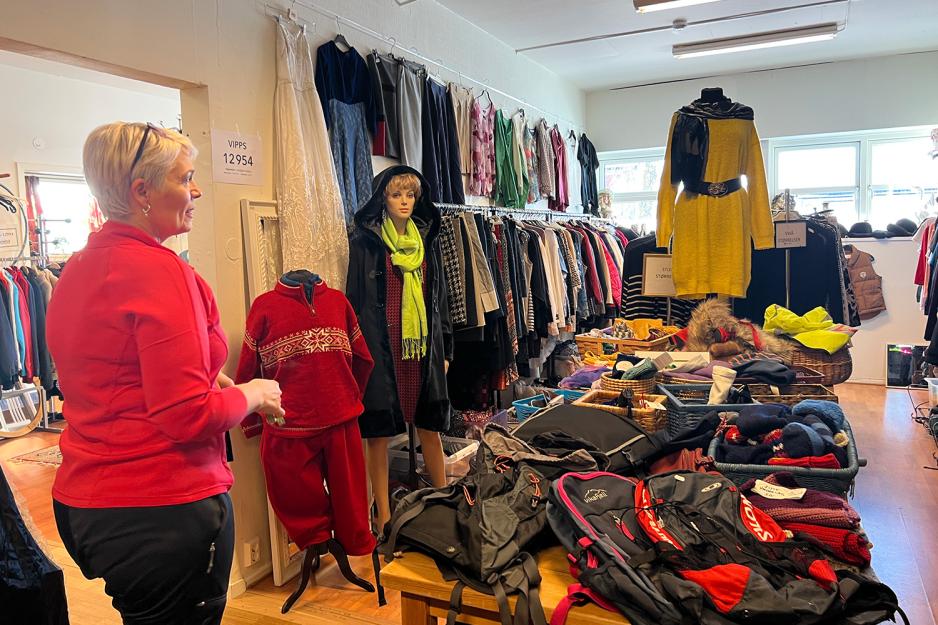 En dame st&aring;r blandt hengere og bord med bruktkl&aelig;r. 