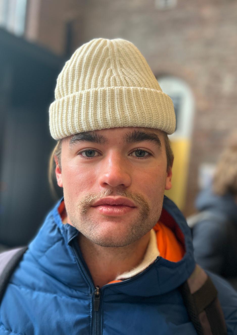 Man med lys og kort bart, lue st&aring;ende opp&aring; hodet, og nlytralt annsiktsuttryk