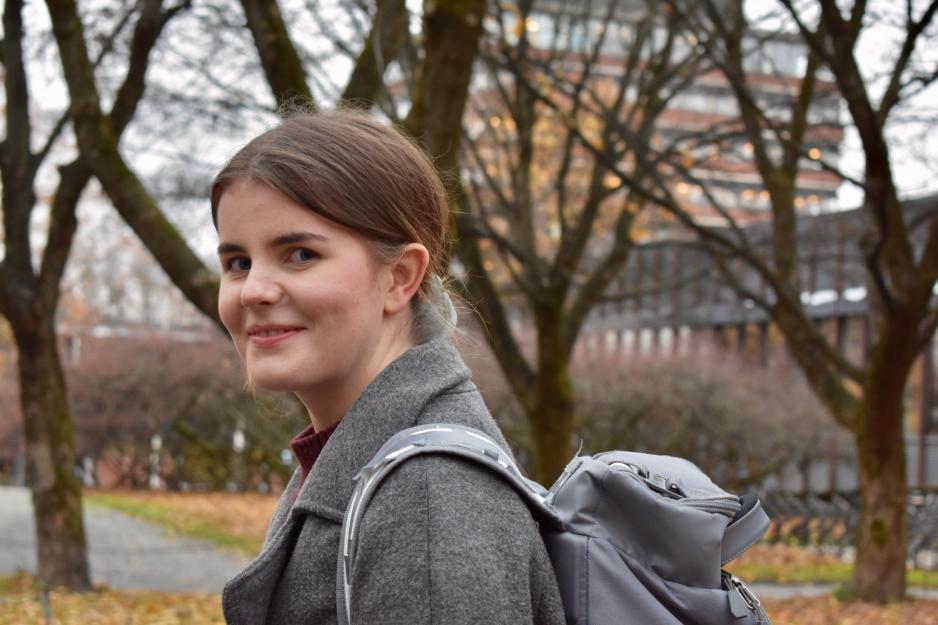 Ung kvinne med m&oslash;rkt h&aring;r og ryggsekk. Tr&aelig;r i bakgrunnen.  