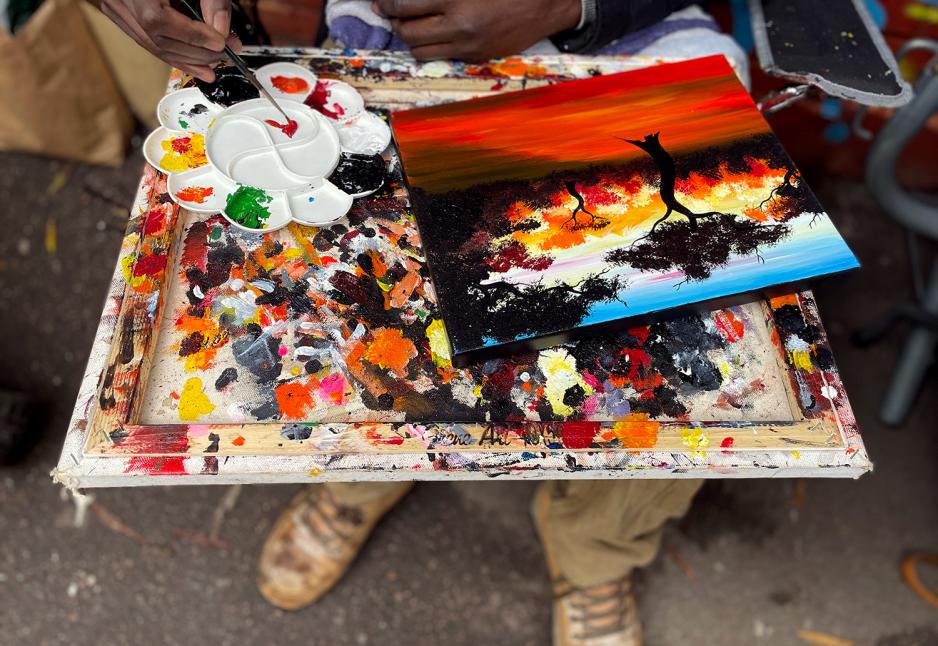 Bildet viser en maler i aksjon. Et landskapsbilde blir til med flotte r&oslash;d og bl&aring; toner. 