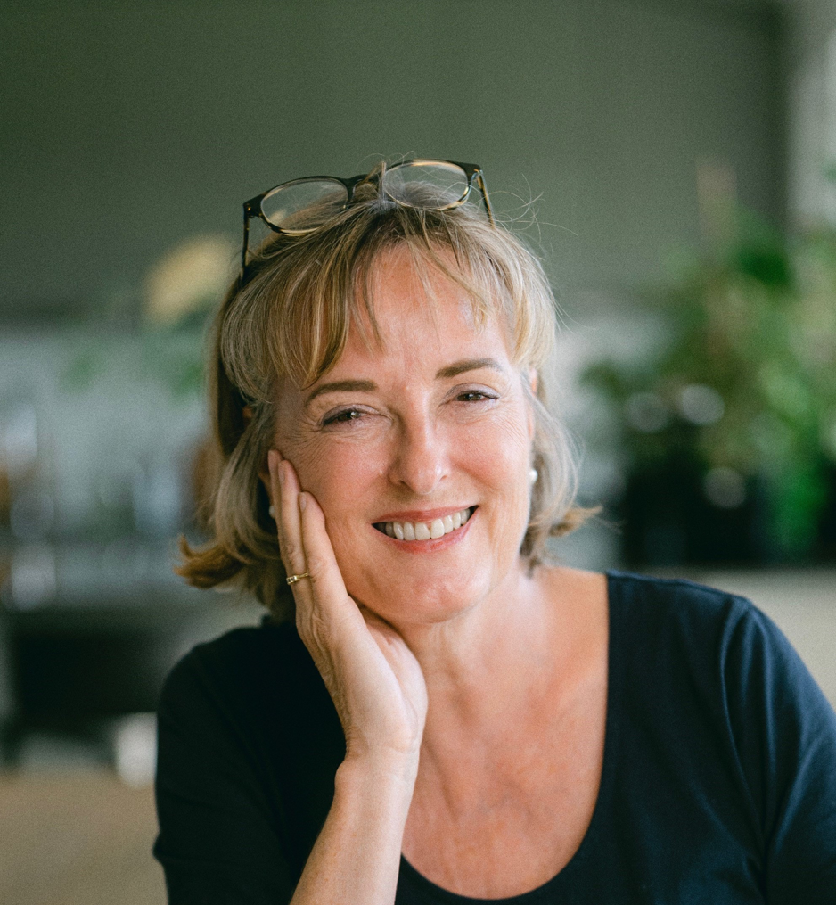 Dame med brunt h&aring;r smiler inn mot kameraet. 