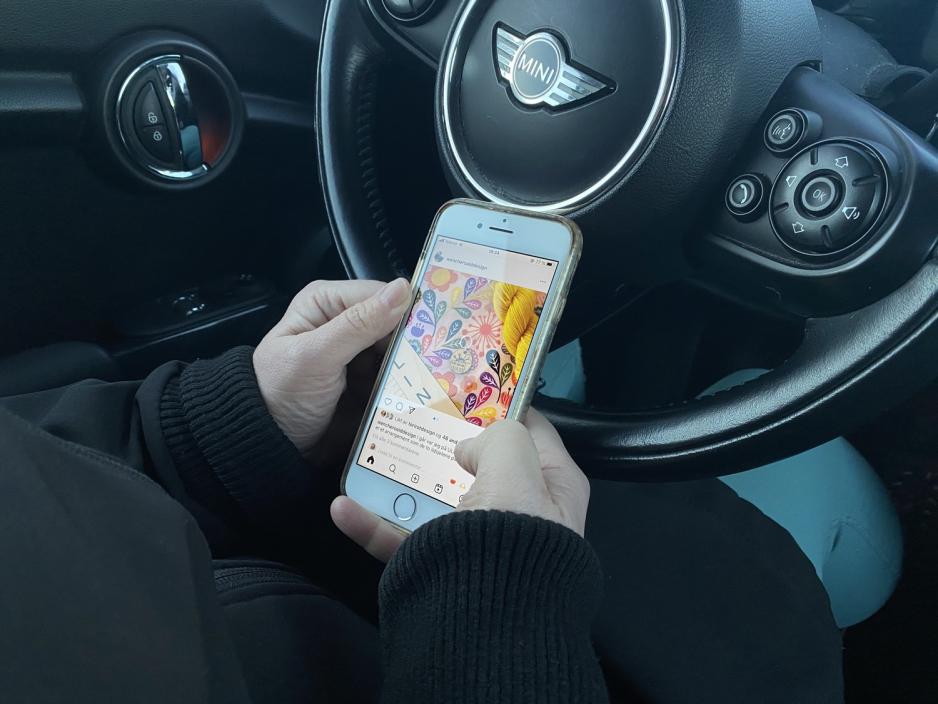 En kvinne har oppe Instagram p&aring; telefonen imens hun sitter bak rattet