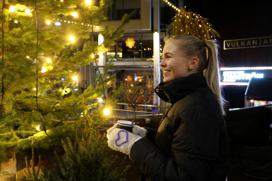 Jente st&aring;r ved juletre og drikker gl&oslash;gg