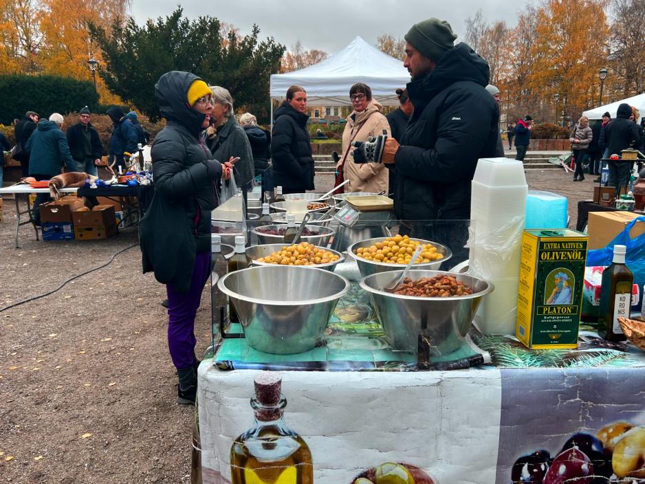 To personer over bord med mat p&aring;, blandt annet poteter, en kvinne til venstre som kj&oslash;per mat og en mannlig selger til h&oslash;yre