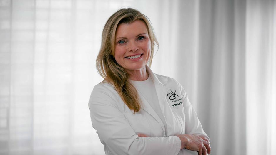 Bilde av en lege som st&aring;r med hender i kryss