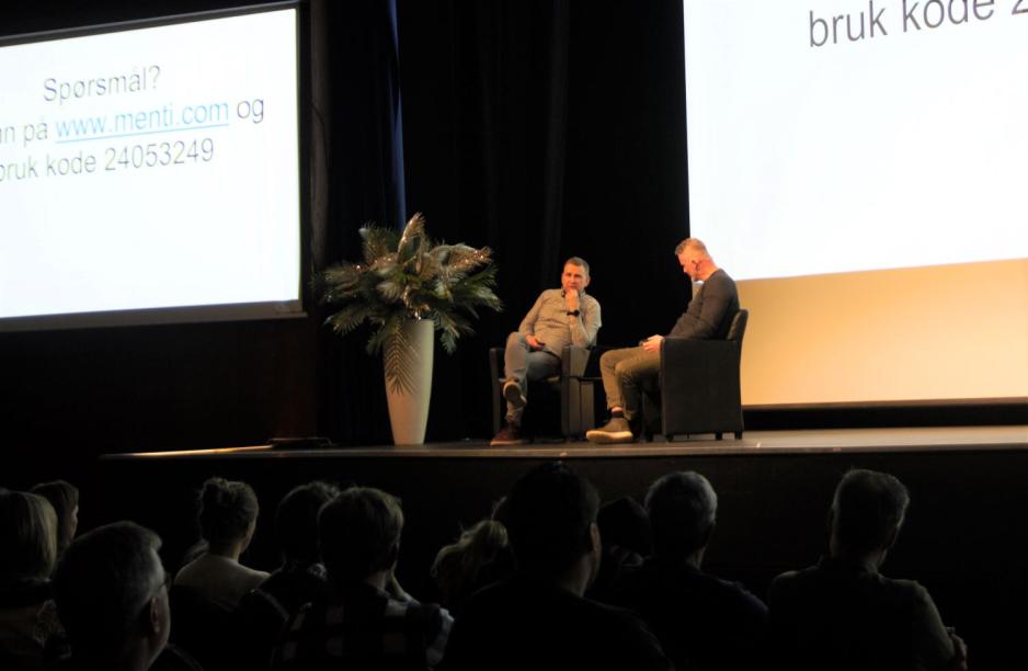 To menn sitter i hver sin skinnstol p&aring; en scene. 