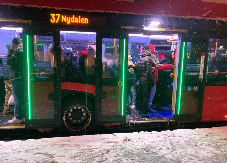 Full buss med passasjerer i linje 37 mot Nydalen. Det sn&oslash;r utenfor, og er sn&oslash; p&aring; bakken. Passasjerene m&aring; st&aring; p&aring; bussen, da det ikke er sitteplasser. 