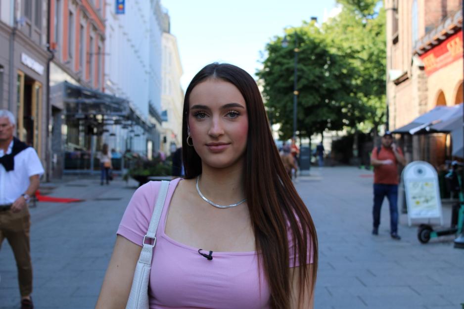 Oda Rikheim, en ung, smilende kvinne med langt brunt h&aring;r, hvit h&aring;ndveske og rosa genser i en gate i Oslo