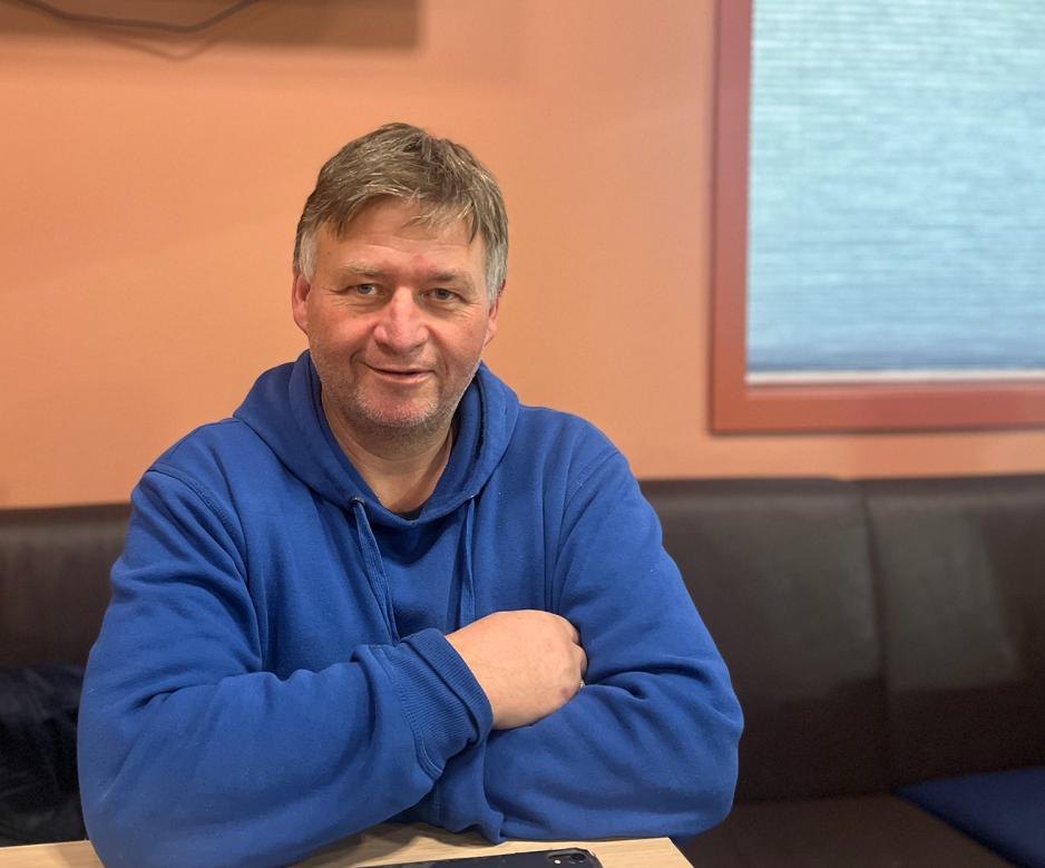 En mann sitter ved et bor med bl&aring; hettegenser og armene i kors. 