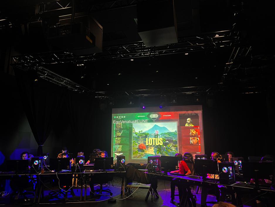 Mange gutter sitter bak hver sin datamaskin og spiller dataspill. En stor skjerm henger ned fra taket, hvor publikum kan f&oslash;lge med p&aring; kampen. 