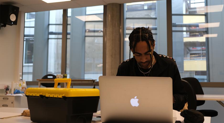 Gutt jobber p&aring; pc med en verkt&oslash;ykasse p&aring; pulten. Han er i et klasserom p&aring; ESMOD Oslo.