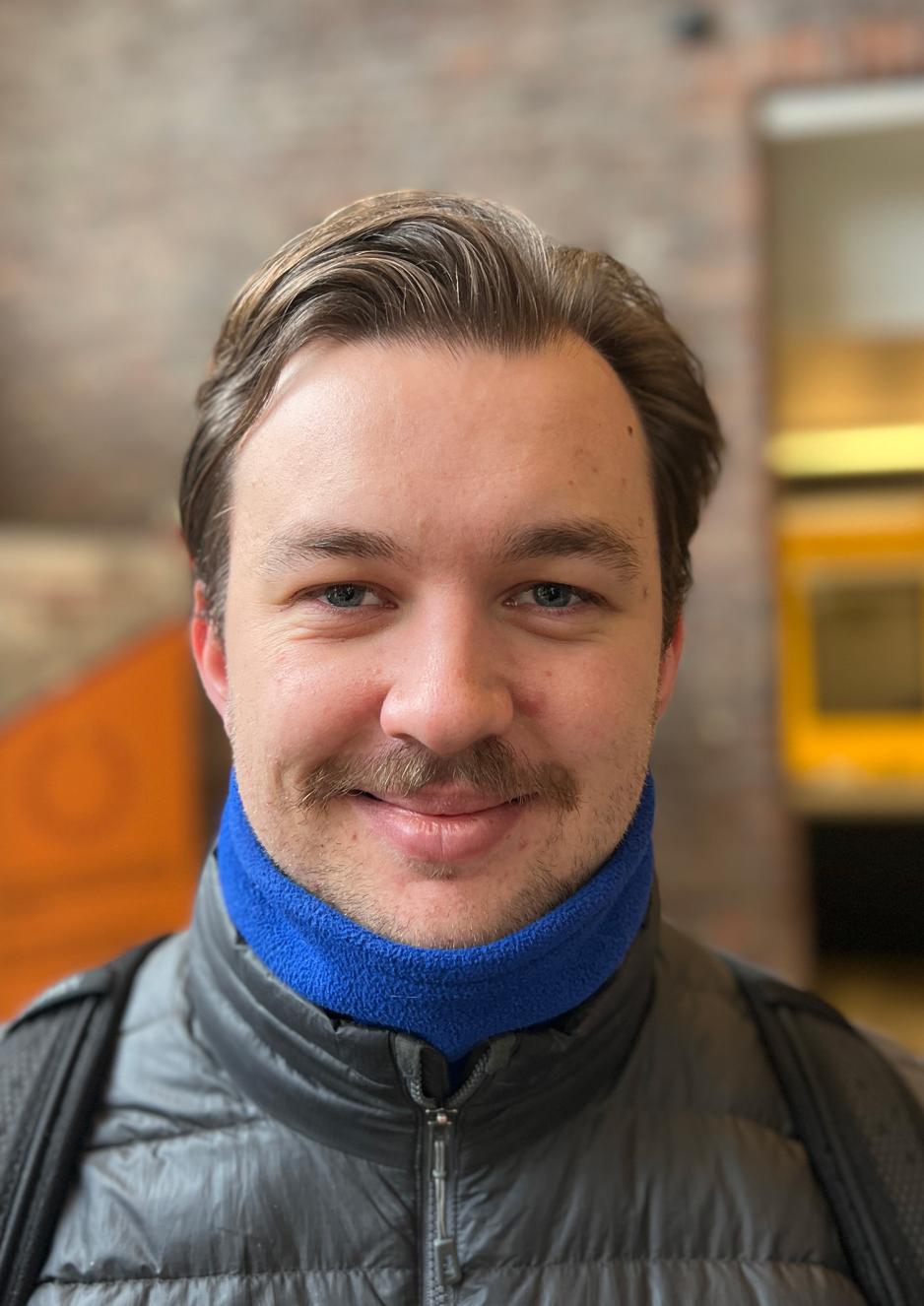 Mann med Fyldig brun bart og brunt h&aring;r. Mildt smil