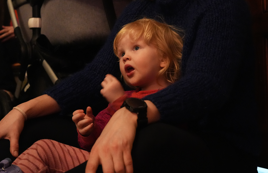 Jente sitter p&aring; mammas fang og ser p&aring; forestilling. 