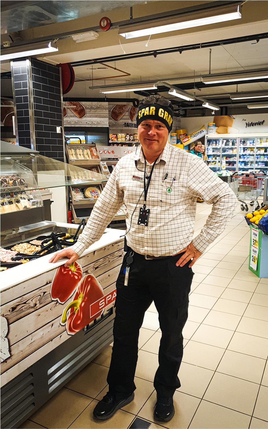 Dagligleder p&aring; spar gran, lener seg inntil salatbaren i butikken og smiler. 